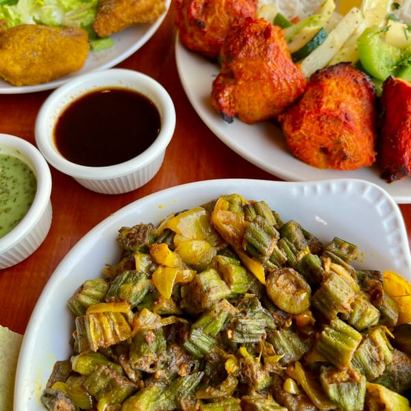 Indian dishes including okra curry, tandoori chicken, and sauces on a wooden table.