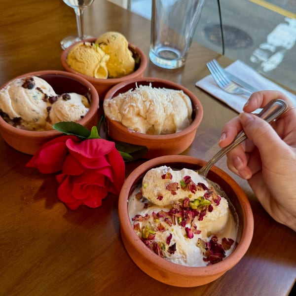 Four bowls of ice cream, one being eaten, with a red rose on a wooden table.