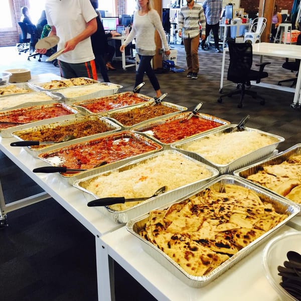 A buffet line with various Indian dishes in foil pans, including rice, curries, and naan.