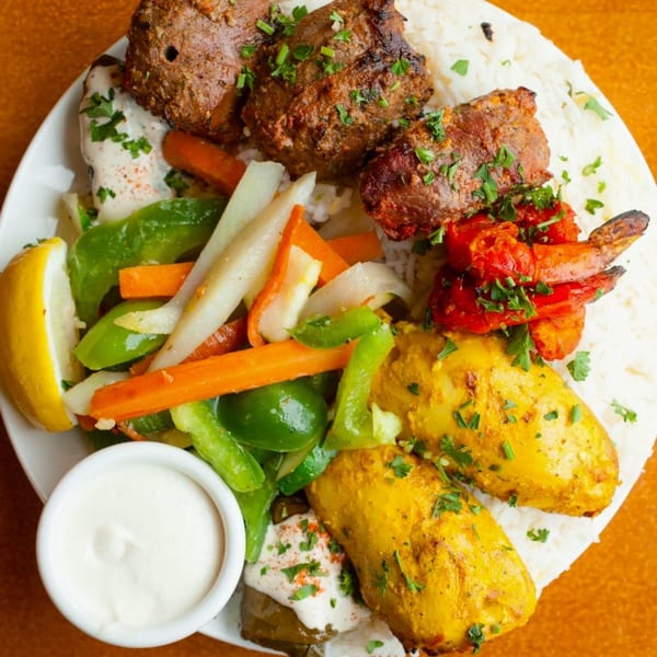 A vibrant Indian platter with grilled meats, chicken, shrimp, rice, vegetables, and dipping sauce.