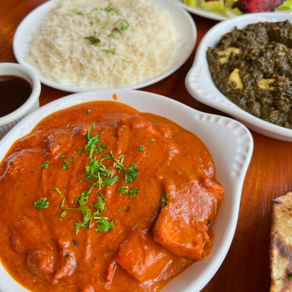 Indian butter chicken, palak paneer, basmati rice, and naan bread on a wooden table.