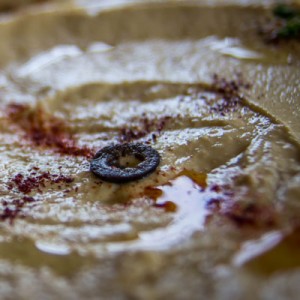 A dish of hummus with spices and an olive in the middle.