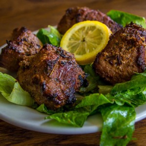 A lamb Shish-kabob with fresh veggies and a lemon.