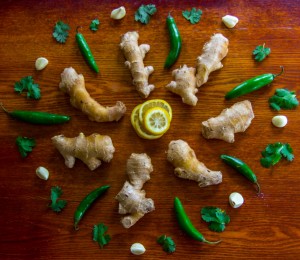 There are fresh lemons, ginger, peppers, garlic, and mint in a circle on a table.