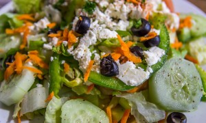 A bowl of Mediterranean salad which has Fresh garden salad made with lettuce, tomatoes, olives, carrots, bell peppers, mushrooms, cucumbers, feta cheese and your choice of either Mediterranean or Ranch dressing.