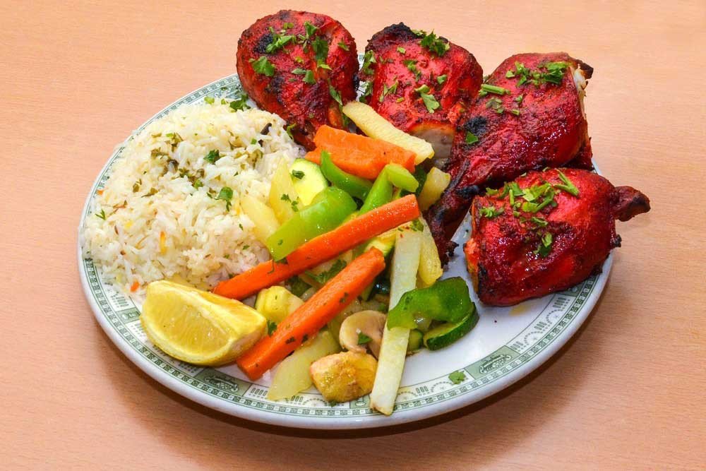 A fresh plate of Tikka Chicken with veggies, rice, and a lemon.