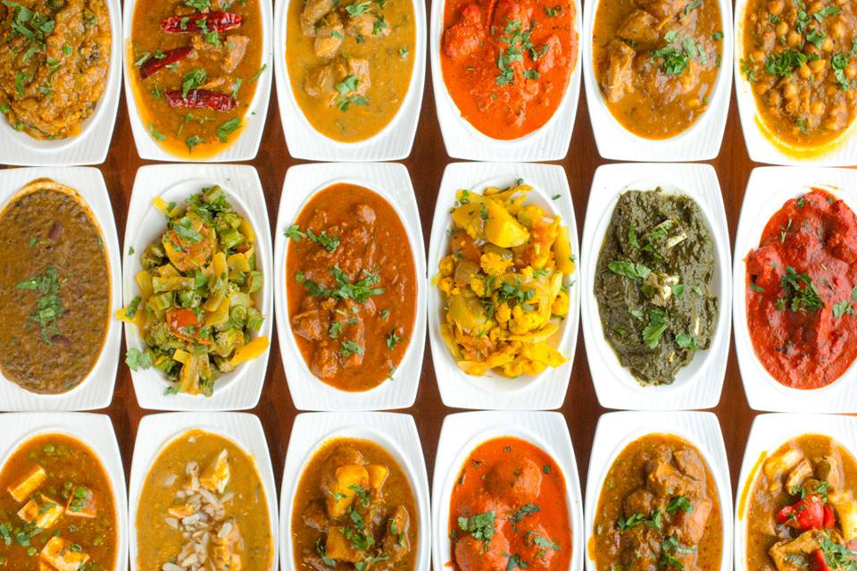 Multiple plates in a row with a variety of Indian and Mediterranean foods.